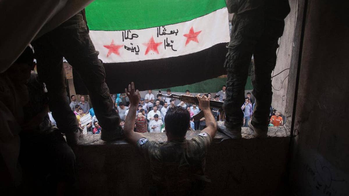 FILE - In this Friday, Sept. 21, 2012 file photo, Free Syrian Army rebels hold a revolutionary flag during a demonstration in the Bustan al-Qasr neighborhood of Aleppo, Syria. A dispute erupted on Tuesday, May 12, 2015, among the Syrian opposition after a press conference where the Khaled Khoja, leader of the Syrian National Coalition, decided not to display the flag that for the past four years many have adopted as the symbol of their rebellion - a green, white and black flag with three red stars - after another opposition figure argued it was divisive. The official Syrian flag is red, white and black with two green stars in the center. Arabic on the flag is reversed, but reads, 