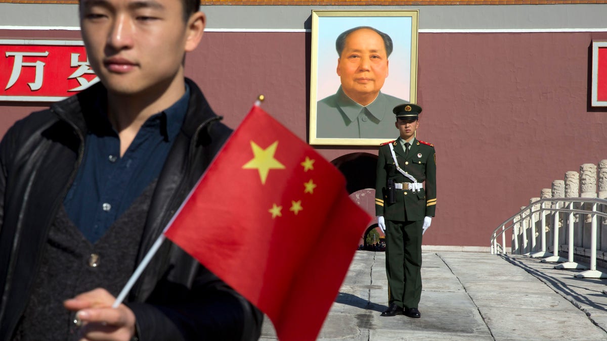A tourist holds up a Chinese flag as he poses for photos near a Chinese paramilitary policeman on duty in front of former Chinese leader Mao Zedong's portrait on Tiananmen Gate, close to the site of an incident Monday where a car plowed through a crowd before it crashed and burned in Beijing, China, Tuesday, Oct. 29, 2013. Police investigating the apparent car attack at Beijing's Forbidden City searched Tuesday for information on two ethnic Uighur minority suspects, a hotel employee said, a day after the incident which killed five people and injured 38.(AP Photo/Ng Han Guan)