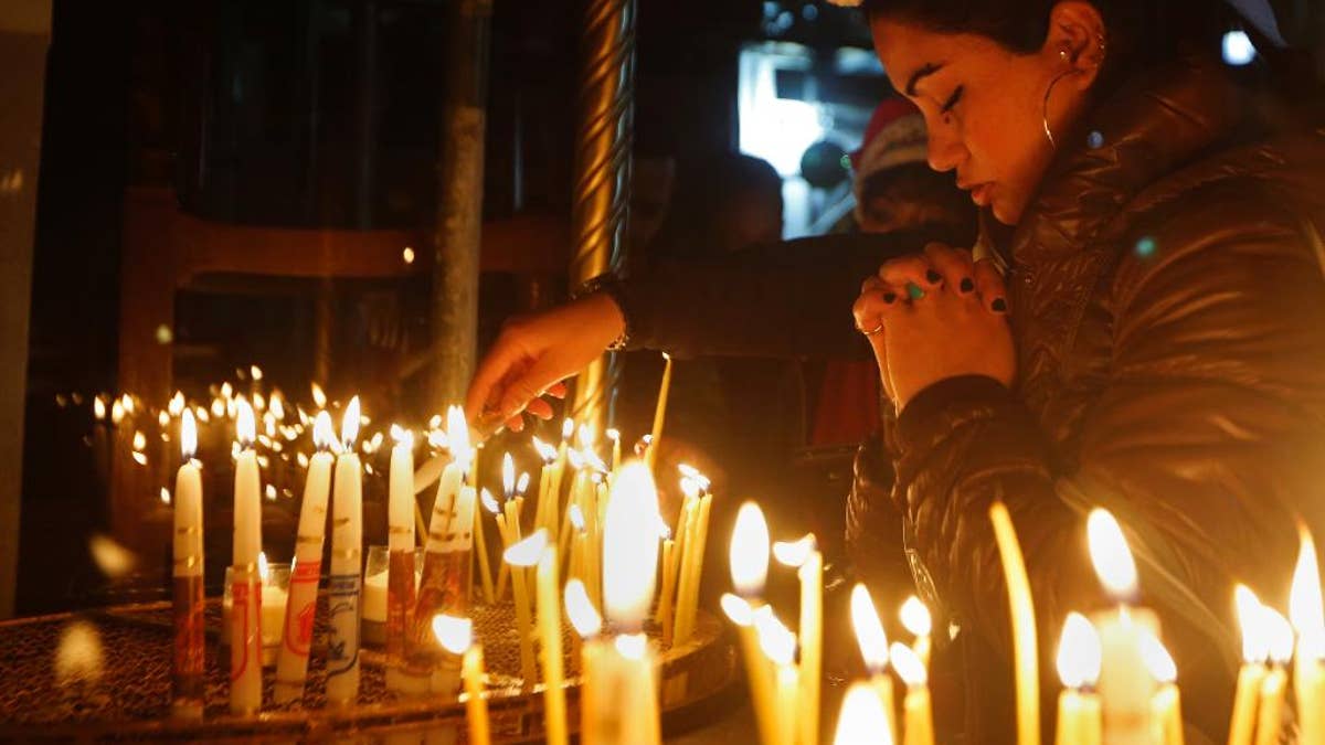 A Christian worshipper prays after lighting a candle on Christmas Eve at the Church of the Nativity, built atop the site where Christians believe Jesus Christ was born, in the West Bank City of Bethlehem, Saturday, Dec. 24, 2016. (AP Photo/Majdi Mohammed)