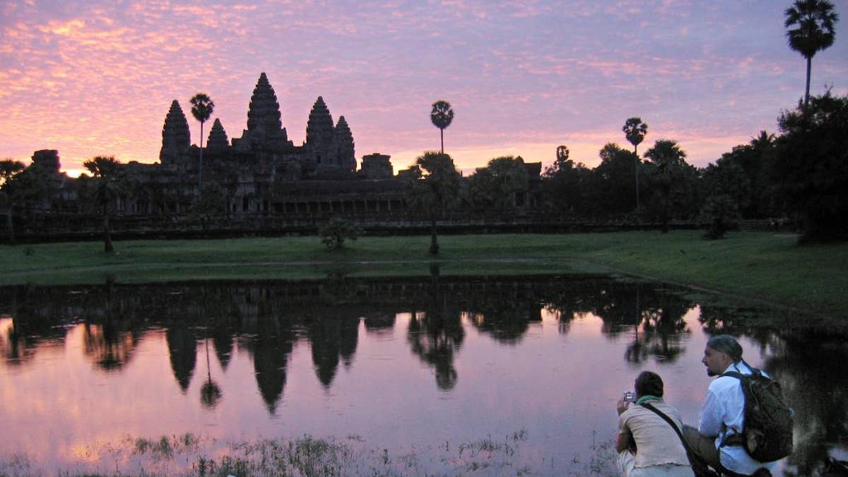 FILE - In this July 14, 2014 file photo, tourists look at the view of the Angkor Wat temples at sunrise, outside Siem Reap, Cambodia. An Australian archeologist says he and colleagues have found evidence of previously undiscovered medieval urban and agricultural networks surrounding the ancient city of Angkor Wat. Using high-tech lasers to scan the Cambodian jungle, Damian Evans and colleagues say they found traces of extensive networks surrounding the monumental stone temple complex at Angkor Wat.  (AP Photo/Anat Givon, File)