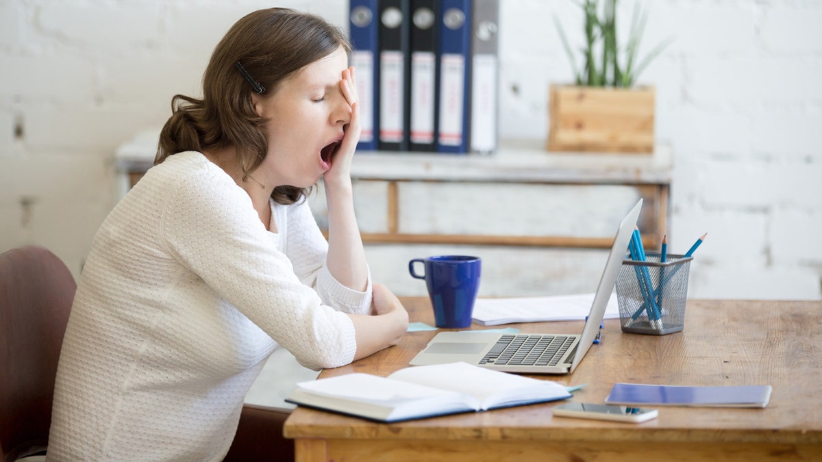 Portrait of young woman sitting at table in front of laptop, sleepy, tired, overworked, lazy to work. Attractive business woman yawning in home office relaxing or bored after work on laptop computer
