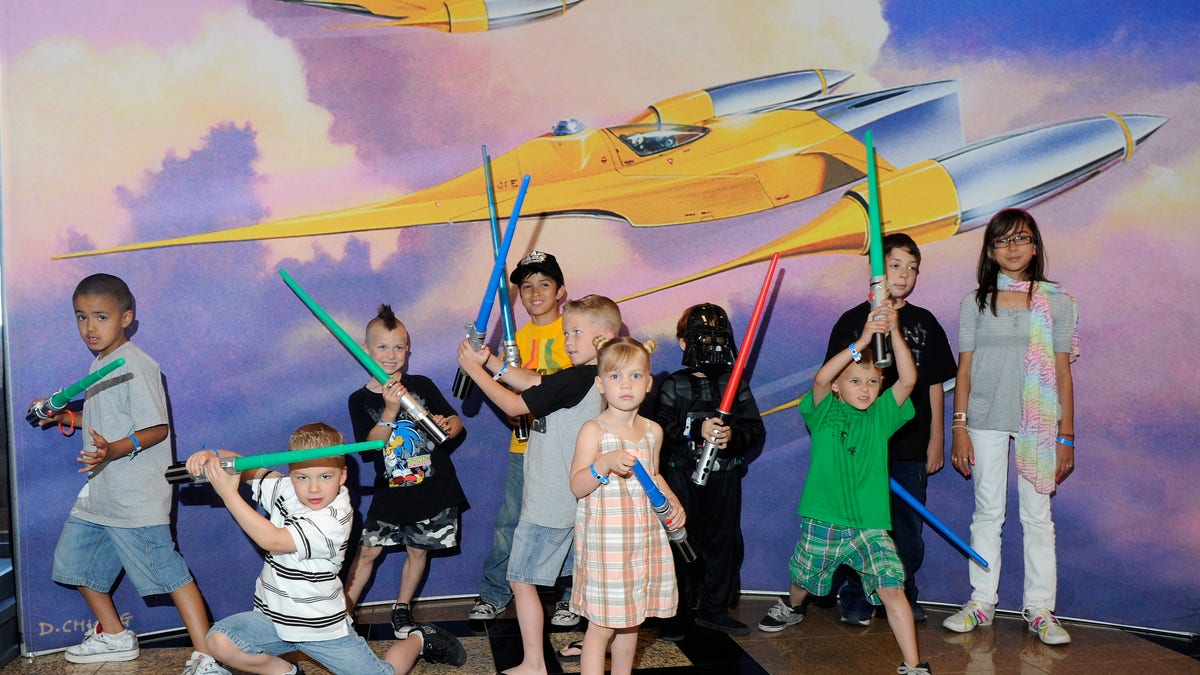 LAS VEGAS - MAY 29: Kids with toy lightsabers pose in front of Star Wars artwork at the museum exhibit of "Star Wars: In Concert" at the Orleans Arena May 29, 2010 in Las Vegas, Nevada. The traveling production features a full symphony orchestra and choir playing music from all six of John Williams' Star Wars scores synchronized with footage from the films displayed on a three-story-tall, HD LED screen. (Photo by Ethan Miller/Getty Images)