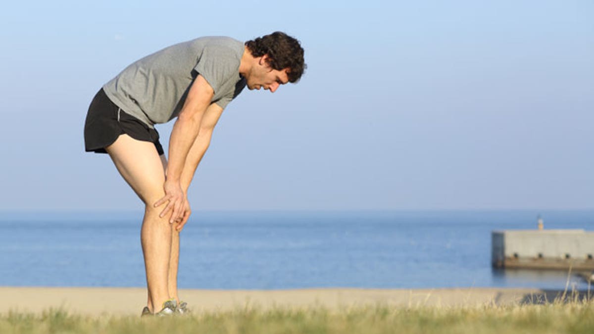 Exhausted runner man resting on the beach after workout