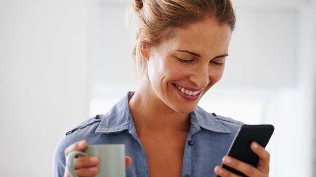 Woman drinking coffee using smartphone at home