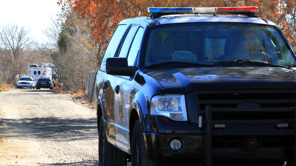 A Bernalillo County sheriff's deputy blocks the dirt road that leads to a home where detectives on Sunday, Jan. 20, 2013, were investigating the deaths of five people who were shot to death south of Albuquerque, N.M. Authorities say a teenager has been arrested and booked on murder and other charges in connection with the shootings. (AP Photo/Susan Montoya Bryan)