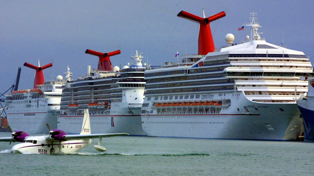 An aircraft lands in front of Carnival cruise ships docked January 6, 2002 at the Port of Miami in Miami, Florida. (Photo by Joe Raedle/Getty Images)