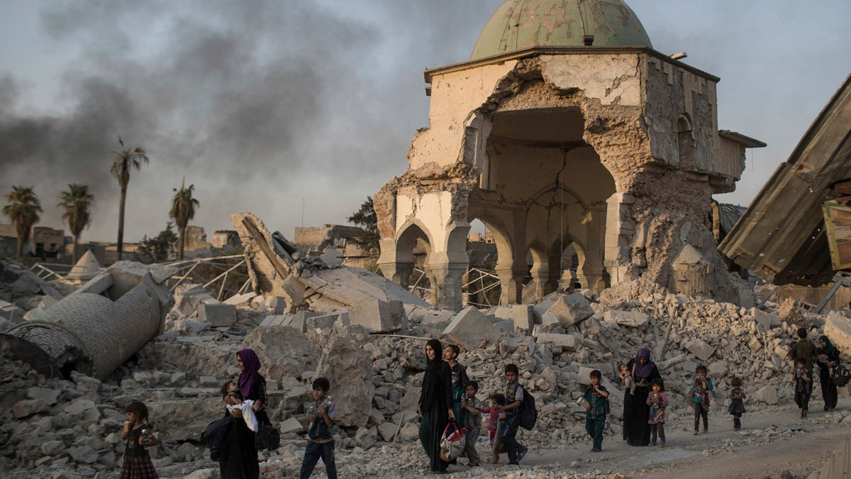 FILE - In this July 4, 2017 file photo, fleeing Iraqi civilians walk past the heavily damaged al-Nuri mosque as Iraqi forces continue their advance against Islamic State militants in the Old City of Mosul, Iraq. A new United Nations report published Thursday, Nov. 2, 2017,  has found that the Islamic State group committed serious 