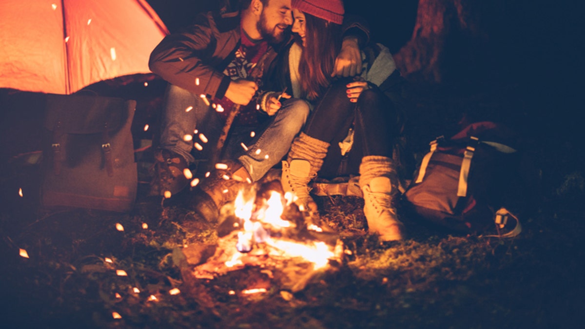 Young couple camping at mountain. Sitting in front of tent and warming by the fire. Wearing warm clothing. Winter night. Austrian Alps