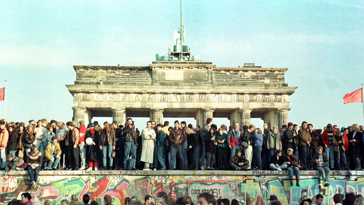 FILE PHOTO 10NOV89 - West Berlin citizens continue their vigil atop the Berlin Wall in front of the Brandeburg Gate in this November 10, 1989 file photo. The 10th anniversary off the "fall" of the Berlin wall is coming up on November 9, 1999. - RTXJABF