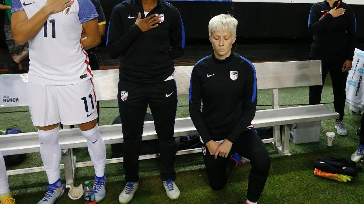 FILE - In this Sunday, Sept. 18, 2016 file photo, United States' Megan Rapinoe, right, kneels next to teammates Ali Krieger (11) and Crystal Dunn (16) as the U.S. national anthem is played before an exhibition soccer match against Netherlands in Atlanta. Megan Rapinoe says she will respect a new U.S. Soccer Federation policy that says national team players 