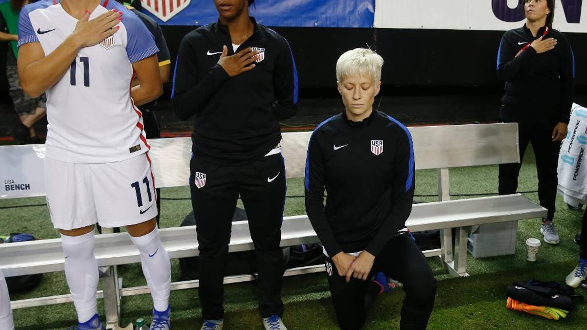 FILE - In this Sunday, Sept. 18, 2016 file photo, United States' Megan Rapinoe, right, kneels next to teammates Ali Krieger (11) and Crystal Dunn (16) as the U.S. national anthem is played before an exhibition soccer match against Netherlands in Atlanta. Megan Rapinoe says she will respect a new U.S. Soccer Federation policy that says national team players 