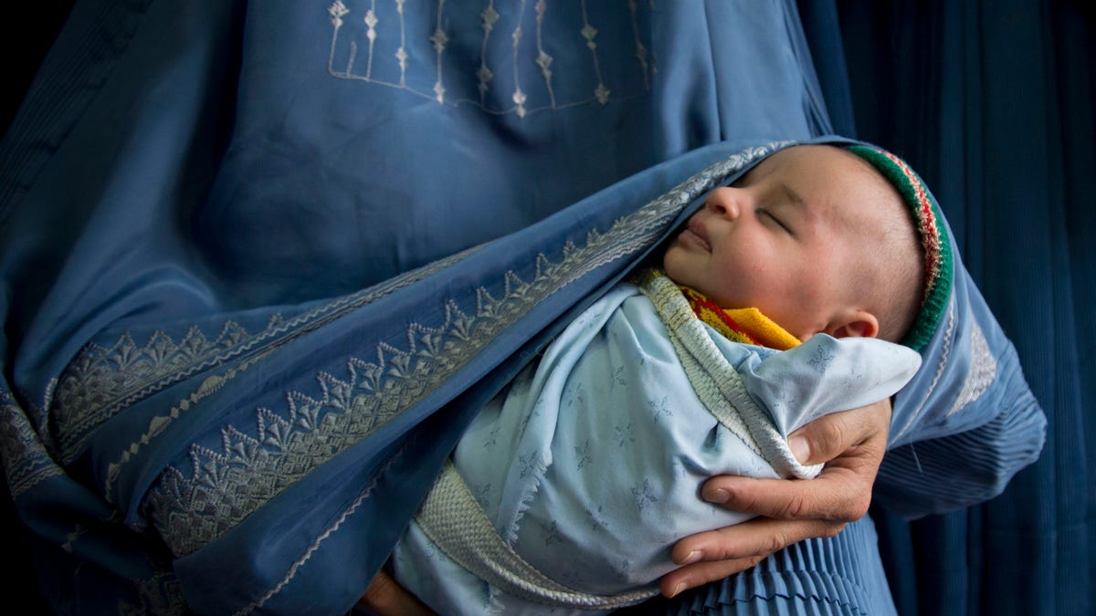 In this Thursday, April 11, 2013 photo, an Afghan woman holds her newly born baby wrapped in her burqa  as she waits to get in line to try on a new burqa in a shop in the old town of Kabul, Afghanistan. Despite advances in womens rights, Afghanistan remains a deeply conservative country and most women continue to wear the Burqa. But tradesmen say times are changing in Kabul at least, with demand for burqas declining as young women going to school and taking office jobs refuse to wear the cumbersome garments. (AP Photo/Anja Niedringhaus)