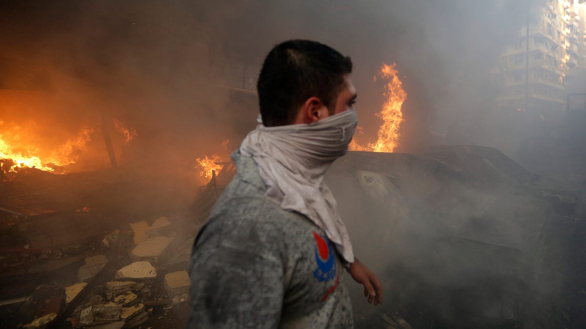 A Hezbollah civil defense worker walks past a burned car at a car bomb in the southern suburb of Beirut, Lebanon, Thursday, Aug. 15, 2013. The powerful car bomb ripped through a southern Beirut neighborhood that is a stronghold of the militant group Hezbollah on Thursday, killing at least three people and trapping others in burning buildings, the media said. (AP Photo/Hussein Malla)