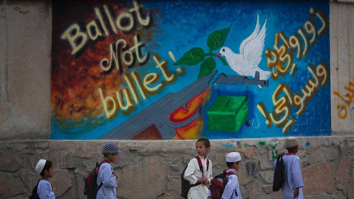Afghan school children walk past a school with graffiti