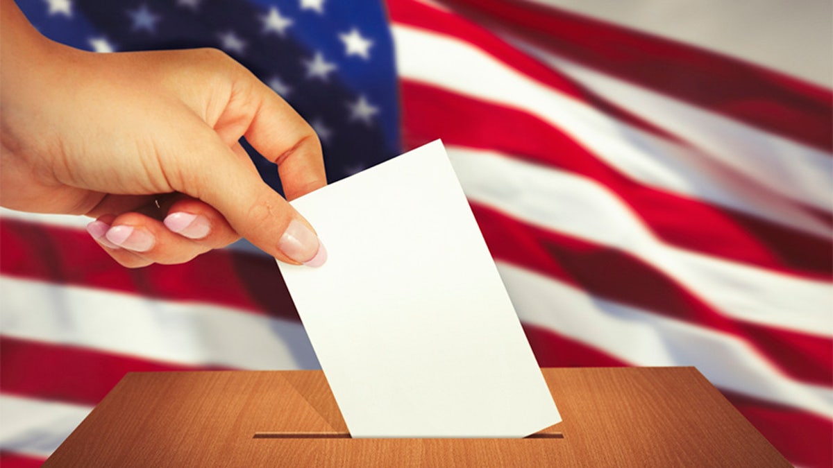 Hand putting a ballot into ballot box with american flag behind