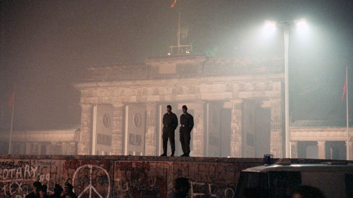 In this Nov. 14, 1989 file photo two East German border guards patrolled atop of Berlin Wall with the illuminated Brandenburg Gate in background, in Berlin. An artist collective plan to rebuild the Berlin wall during an art project in Berlin in October. (AP Photo/Jockel Finck, file)