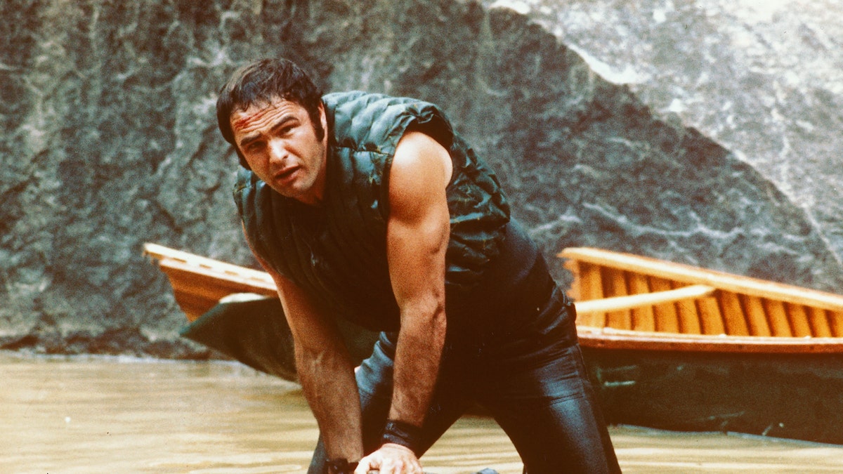 Burt Reynolds, US actor, holding onto some rocks as he struggles in the water with his boat behind him in a publicity still issued for the film, 'Deliverance', USA, 1972, The 1972 thriller, directed by John Boorman, starred Reynolds as 'Lewis Medlock'. (Photo by Silver Screen Collection/Getty Images)