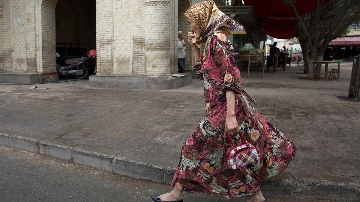 In this photo taken Wednesday, July 16, 2014, a Uighur woman walks past a mosque in the city of Kuqa in western China's Xinjiang province. In China's restive western province of Xinjiang, young men of the Uighur ethnic minority are not allowed to have beards. Also proscribed are certain types of women's headscarves, veils and 