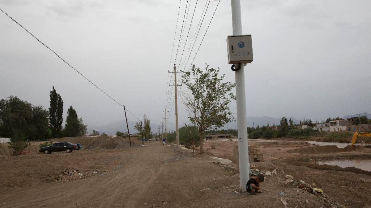 In this photo taken Wednesday, July 16, 2014, a child plays under police surveillance cameras set up to monitor a dirt road intersection in Kuqa in western China's Xinjiang province. China has blanketed parts of Xinjiang, home to Muslim, Turkic-speaking Uighurs, with such heavy security that it resembles an occupied territory under martial law, complete with armed troops, spiked barricades, checkpoints and even drones. But the massive security effort has not brought stability to Xinjiang, and neither has Beijing’s strategy of pouring in economic investment. A few hundred people have died in ethnic violence in Xinjiang and in two attacks in Chinese cities elsewhere over the past 16 months.  (AP Photo/Ng Han Guan)