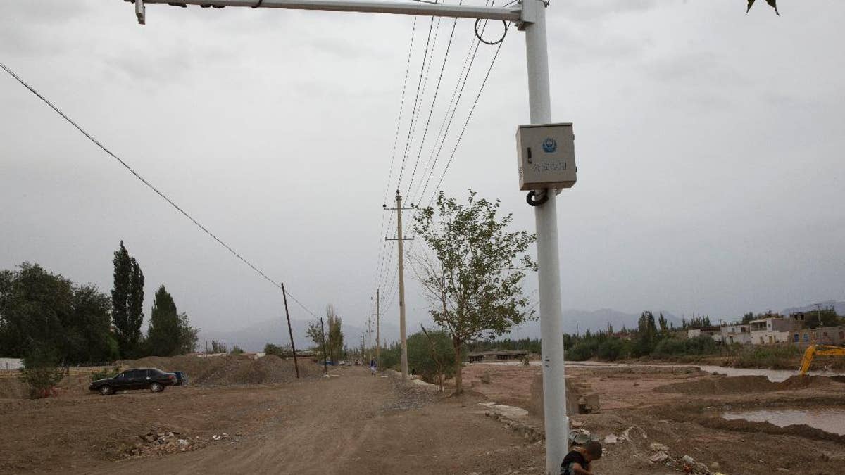 In this photo taken Wednesday, July 16, 2014, a child plays under police surveillance cameras set up to monitor a dirt road intersection in Kuqa in western China's Xinjiang province. China has blanketed parts of Xinjiang, home to Muslim, Turkic-speaking Uighurs, with such heavy security that it resembles an occupied territory under martial law, complete with armed troops, spiked barricades, checkpoints and even drones. But the massive security effort has not brought stability to Xinjiang, and neither has Beijing’s strategy of pouring in economic investment. A few hundred people have died in ethnic violence in Xinjiang and in two attacks in Chinese cities elsewhere over the past 16 months.  (AP Photo/Ng Han Guan)