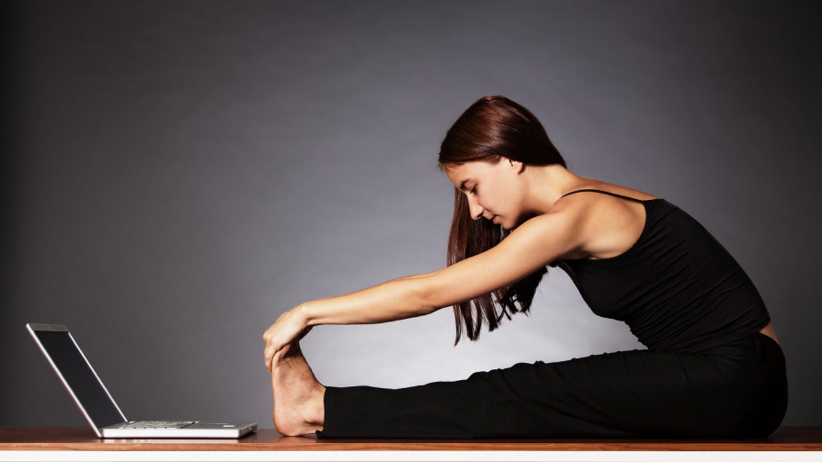 Woman stretching in fornt of laptop.