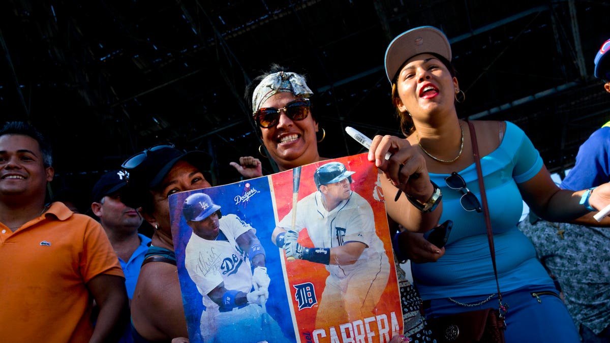 Fans hold photos of MLB players, Cuba's Yasiel Puig, left, and Venezuela's Miguel Cabrera before the players hold a baseball clinic with children in Havana, Cuba, Wednesday, Dec. 16, 2015, during a three-day mission meant to warm relations between Major League Baseball and Cuba. Major League Baseball Players Association executives said they were optimistic about sealing a deal by early next year for the Tampa Bay Rays to play two spring training games in Cuba. They also hope to make progress in one day creating a legal route for Cuban players to make their way to the major leagues. (AP Photo/Ramon Espinosa)