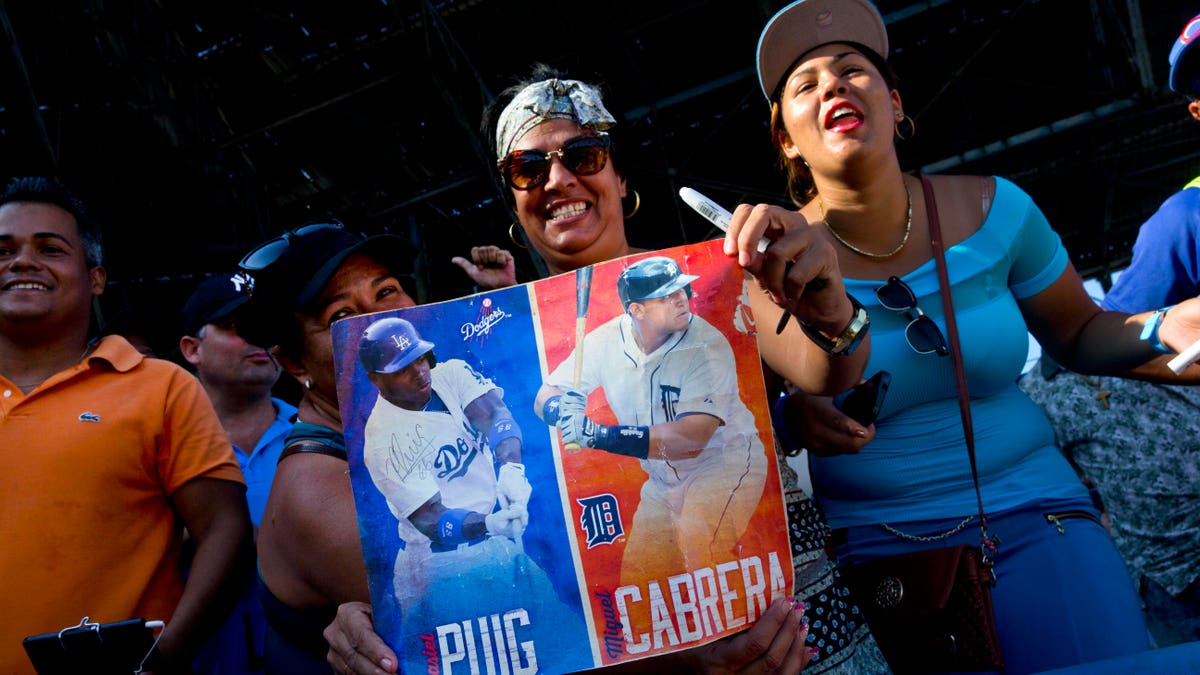 Fans hold photos of MLB players, Cuba's Yasiel Puig, left, and Venezuela's Miguel Cabrera before the players hold a baseball clinic with children in Havana, Cuba, Wednesday, Dec. 16, 2015, during a three-day mission meant to warm relations between Major League Baseball and Cuba. Major League Baseball Players Association executives said they were optimistic about sealing a deal by early next year for the Tampa Bay Rays to play two spring training games in Cuba. They also hope to make progress in one day creating a legal route for Cuban players to make their way to the major leagues. (AP Photo/Ramon Espinosa)