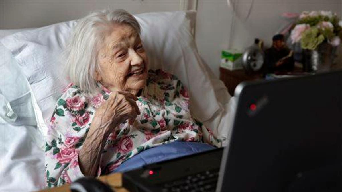 Patient Louise Irving watches a laptop computer with her daughter's morning wake-up video playing, at The Hebrew Home of Riverdale, in New York, Wednesday, March 25, 2015. The nursing home in the Bronx has started a pilot program in which relatives record video messages for patients of Alzheimer's and other forms of dementia. The videos are played for them each morning to calm their agitation and reassure them about their surroundings and their routines.
