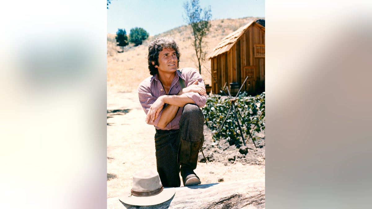 Michael Landon (1936-1991), US actor, poses with his arms crossed and resting on his knee with a log cabin the background in a portrait issued as publicity for the US television series, 'Little House on the Prairie', circa 1974. The drama, adapted from the novels by Laura Ingalls Wilder (1867-1957), starred Landon as 'Charles Ingalls'. (Photo by Silver Screen Collection/Getty Images)