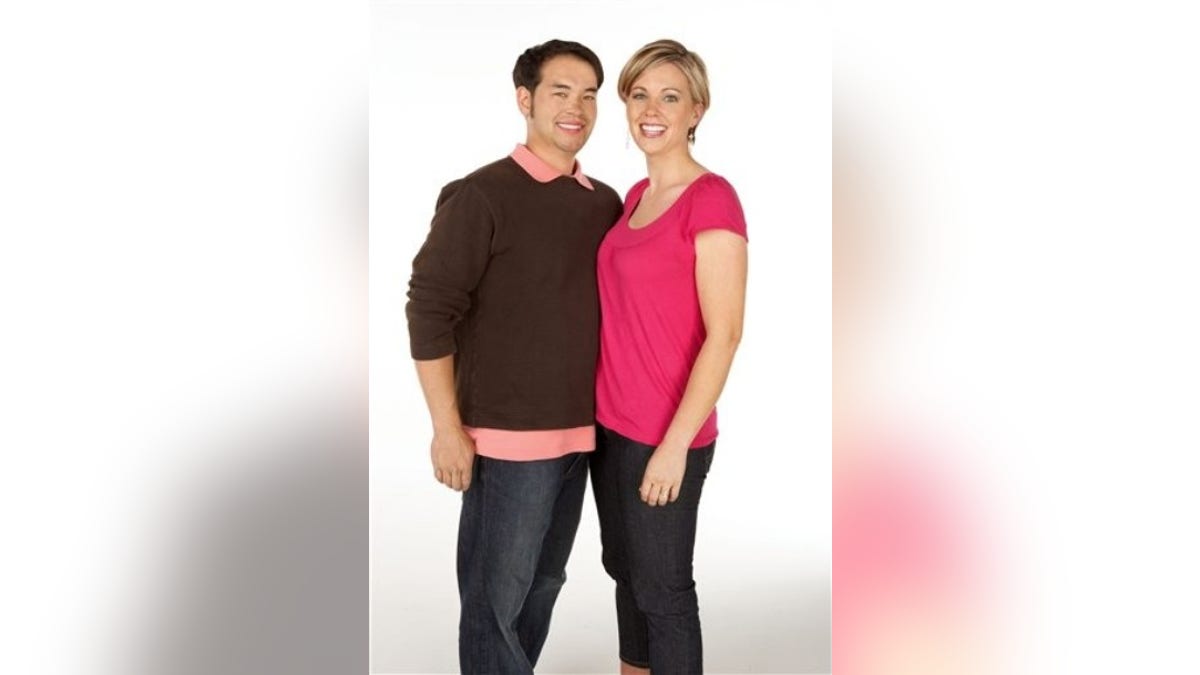 Jon Gosselin wears a brown sweater and smiles next to wife Kate Gosselin in a bright pink shirt