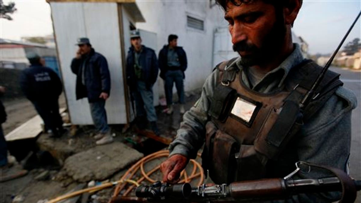 An Afghan policeman with blood in his hand and badge adjusts his gun as others take cover close to the site of a attack in Kabul, Afghanistan on Wednesday, Oct. 28, 2009. Gunmen with automatic weapons and suicide vests stormed a guest house used by U.N. staff in the heart of the Afghan capital early Wednesday, officials said. A Taliban spokesman claimed responsibility, saying it was meant as an assault on the upcoming presidential election. (AP Photo/ Gemunu Amarasinghe)