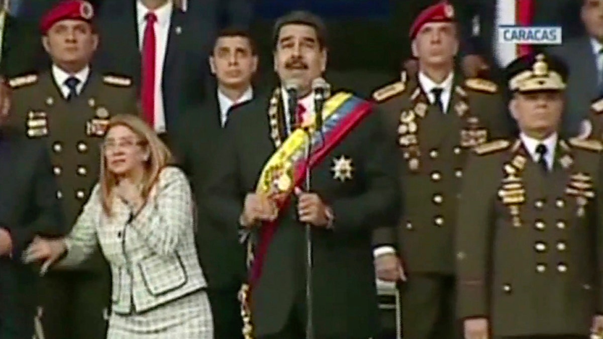 Presiden Nicolas Maduro, center, delivers his speech as his wife Cilia Flores winces and looks up after being startled by and explosion