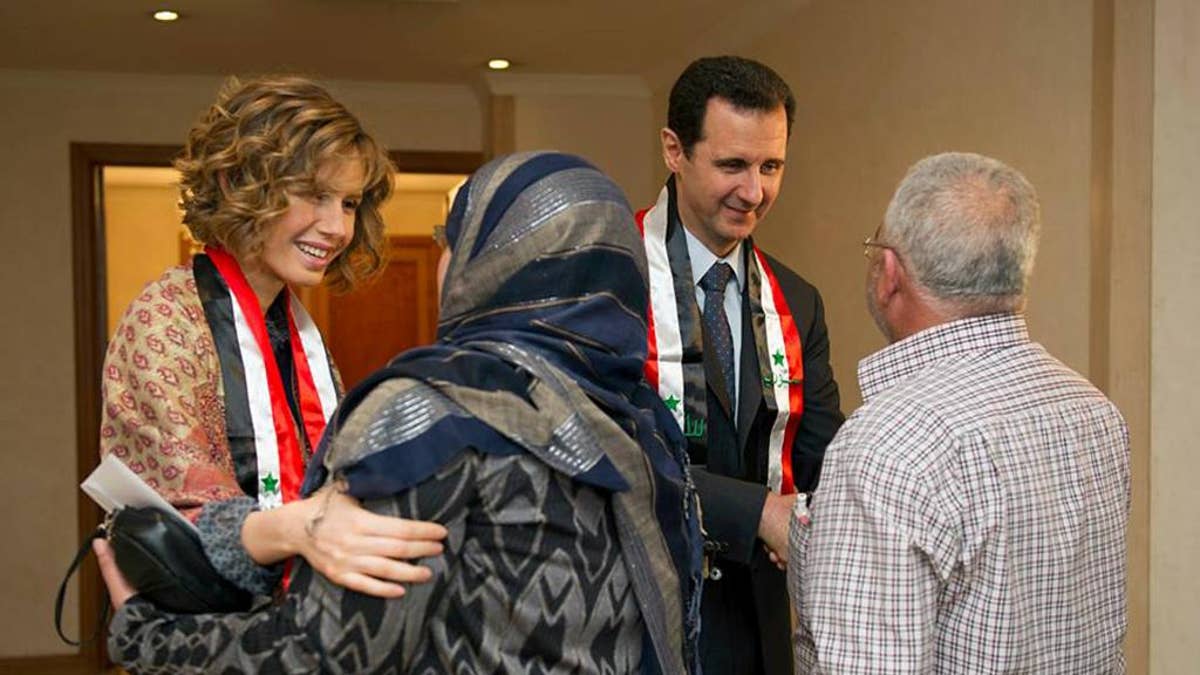 This photo taken on March 20, 2014, posted on the official Facebook page of the Syrian Presidency, shows first lady Asma Assad, left background, and Syrian President Bashar Assad, right background, shaking hands with Syrian teachers in Damascus, Syria. As Syrian army made gains on the battlefield, Assad's Britain-born wife has come out of seclusion, joining her husband's campaign to infuse confidence and optimism into the war-wrecked nation. Since January, Asma Assad has made several carefully scripted public appearances in the past months. (AP Photo/Syrian Presidency via Facebook)