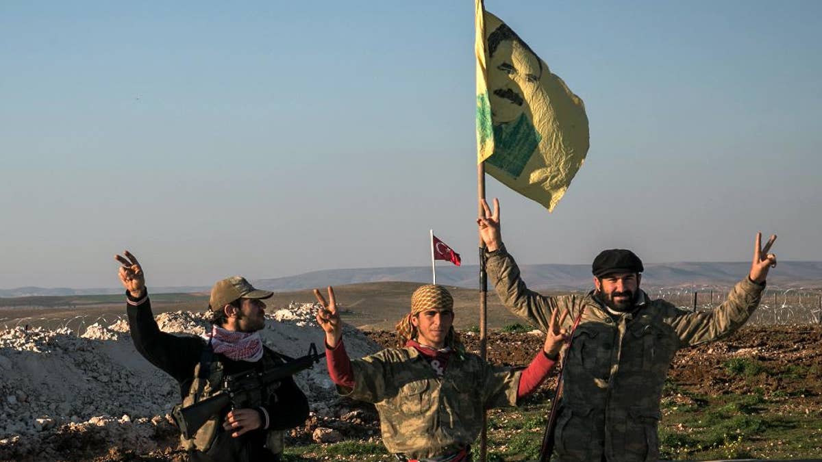 FILE - In this Sunday, Feb. 22, 2015, file photo, Syrian Kurdish militia members of YPG make a V-sign next to poster of Abdullah Ocalan, jailed Kurdish rebel leader, and a Turkish army tank in the background in Esme village in Aleppo province, Syria. Turkish jets struck camps belonging to Kurdish militants in northern Iraq Friday and Saturday in what were the first strikes since a peace deal was announced in 2013. The strikes in Iraq targeted the Kurdistan Workers' Party, or PKK, whose affiliates have been effective in battling the Islamic State group. (AP Photo/Mursel Coban, Depo Photos, File)