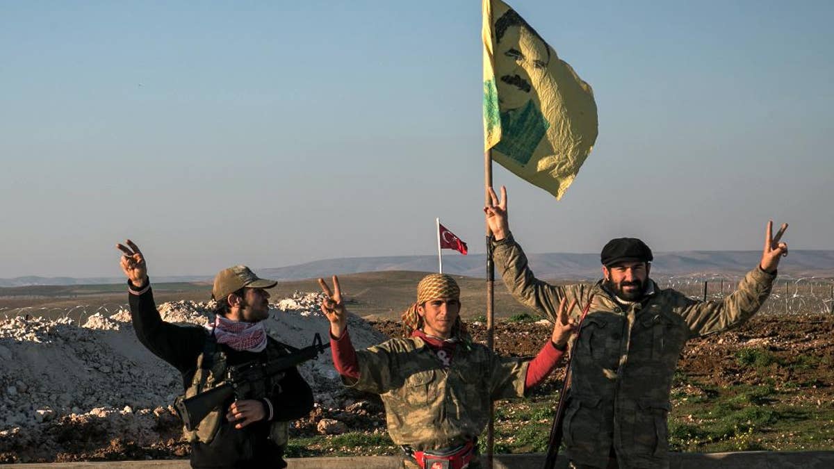 FILE - In this Sunday, Feb. 22, 2015, file photo, Syrian Kurdish militia members of YPG make a V-sign next to poster of Abdullah Ocalan, jailed Kurdish rebel leader, and a Turkish army tank in the background in Esme village in Aleppo province, Syria. Turkish jets struck camps belonging to Kurdish militants in northern Iraq Friday and Saturday in what were the first strikes since a peace deal was announced in 2013. The strikes in Iraq targeted the Kurdistan Workers' Party, or PKK, whose affiliates have been effective in battling the Islamic State group. (AP Photo/Mursel Coban, Depo Photos, File)