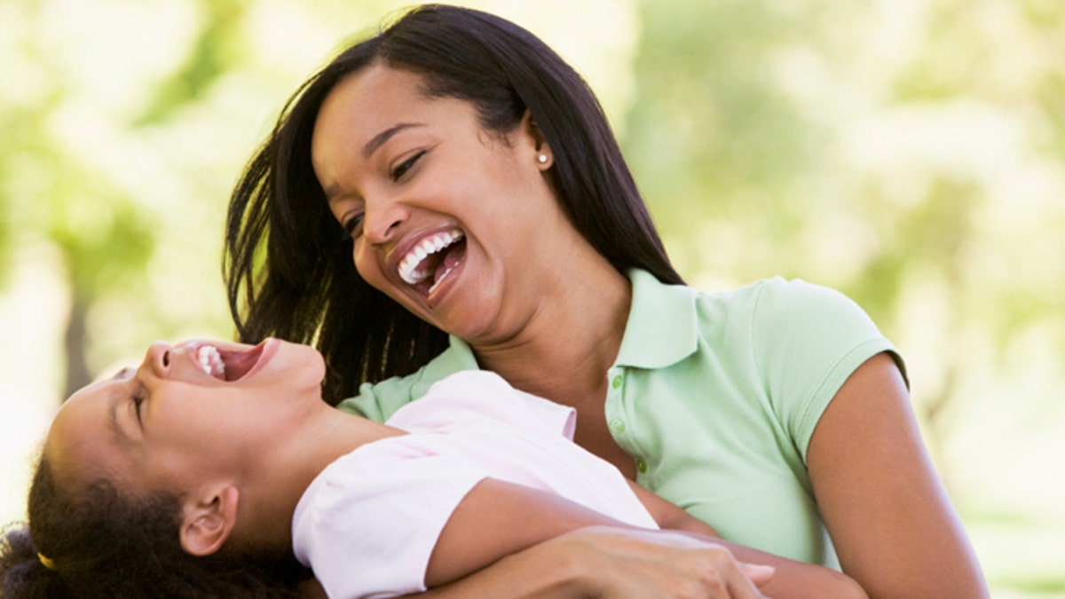 Woman and young girl outdoors embracing and laughing