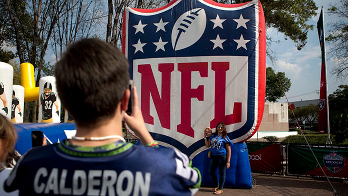 In this Nov. 6, 2016 photo, fans take photos by the NFL logo set up at the third annual American Football Expo in Mexico City. Football, or âfutbol Americano,â has a century-old tradition in Mexico and is one of the most popular sports in the country, where millions of fans follow the action on TV every Sunday. (AP Photo/Eduardo Verdugo)