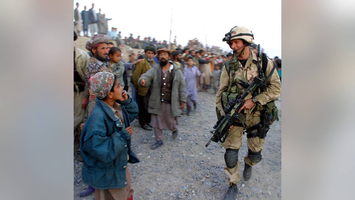 A U.S. Air Force special operations soldier walks by an Afghan boy as others loyal to the northern alliance look on, in Khwaja Bahuaddin, Afghanistan, Thursday, Nov. 15, 2001. Two helicopters with small U.S. Special Forces teams provided security for Andrew Natsios, the director of U.S. Agency for International Development, who visited the longtime northern alliance stronghold to review projects funded by the U.S. aid agency. (AP Photo/Brennan Linsley, Pool)