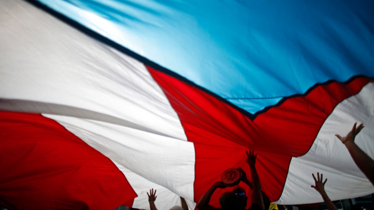 FILE - In this Jan. 15, 2014 file photo, demonstrators touch a giant Puerto Rican flag from underneath as they protest at the labor department during a teachers strike in San Juan, Puerto Rico. From the intriguing to the impossible, there is no shortage of ideas for fixing Puerto Ricos ailing economy as the government tries to dig out from a whopping $70 billion in public debt and bring back economic growth. (AP Photo/Ricardo Arduengo, File)