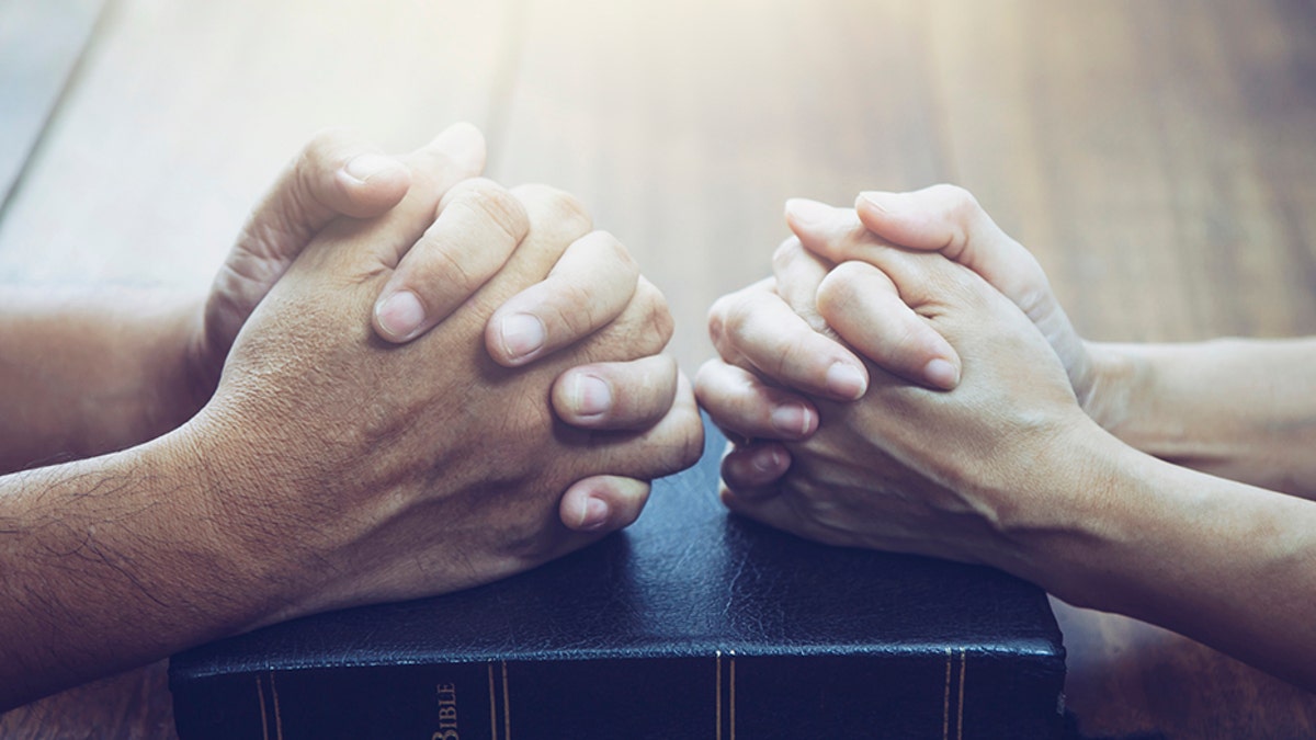 husband and wife are praying together over holy bible on wooden table with the light from above with copy space for your text