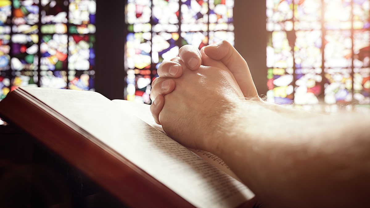 Hands folded in prayer on a Holy Bible in church concept for faith, spirtuality and religion