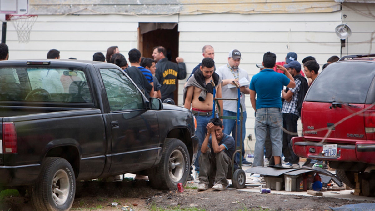 People wait outside a house, Wednesday, March 19, 2014, in southeast Houston. A house overflowing with more than 100 people presumed to be in the United States illegally was uncovered just outside Houston on Wednesday, a police spokesman said. The suspected stash house was found during a search for a 24-year-old woman and her two children that were reported missing by relatives Tuesday after a man failed to meet them, said a spokesman for the Houston Police Department. (AP Photo/Houston Chronicle, Cody Duty)