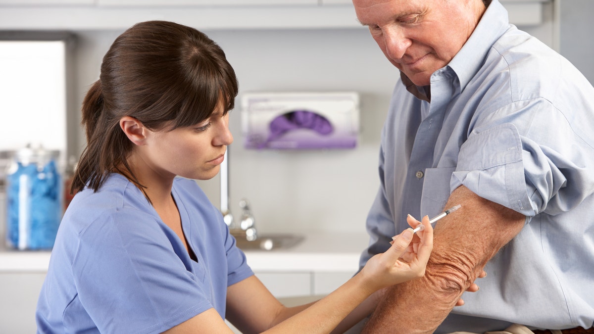 Doctor Giving Male Patient Injection In Hospital Room