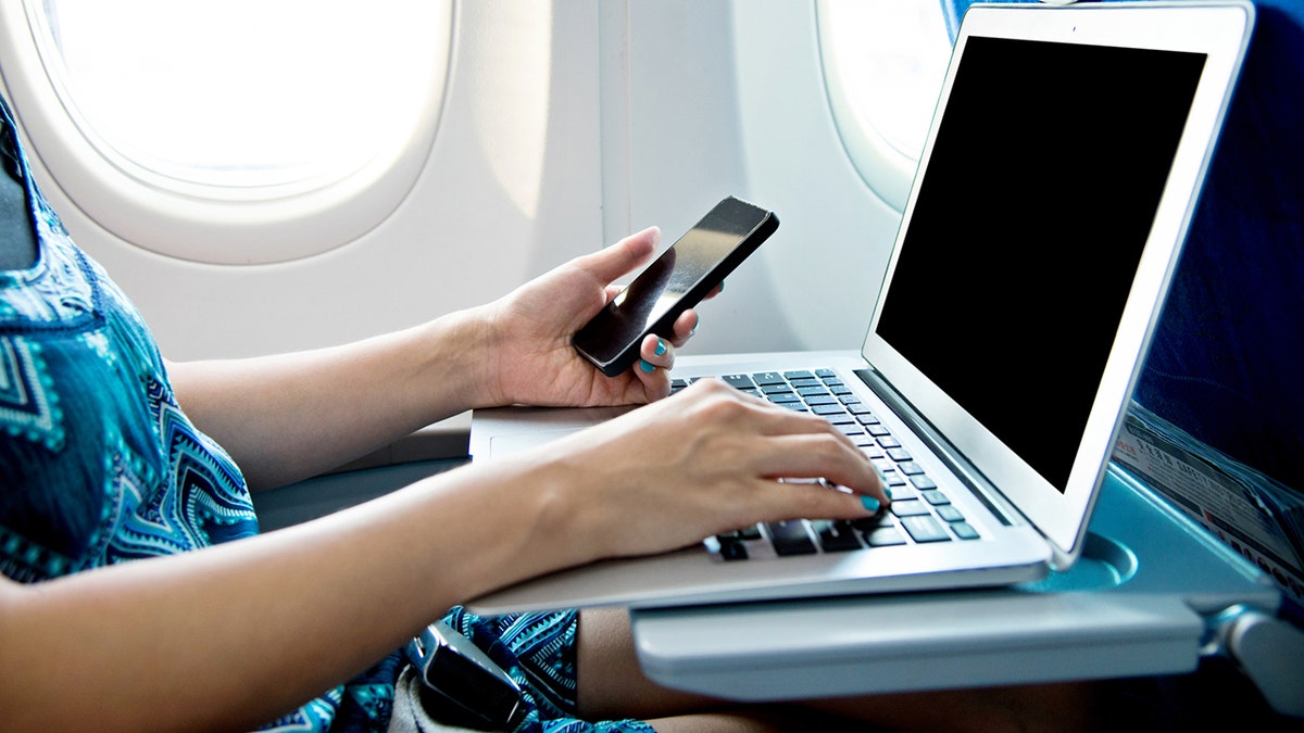 Woman using smart phone and laptop on airplane.