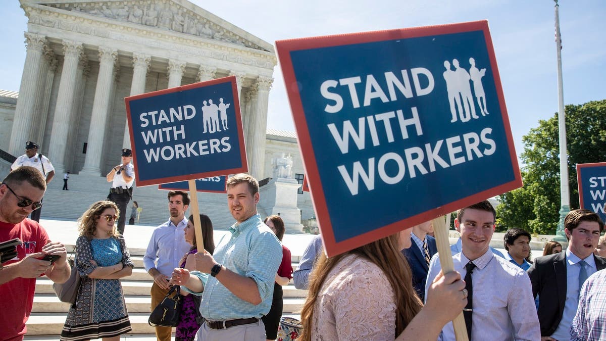 FILE - In this Monday, June 25, 2018 file photo, people gather at the Supreme Court awaiting a decision in an Illinois union dues case, Janus vs. AFSCME, in Washington. An Oregon state employee and a labor union have reached a settlement over her lawsuit seeking payback of obligatory union fees, marking the first refund of forced fees since the U.S. Supreme Court ruled in late June that government workers can't be required to contribute to labor groups, the employee's lawyers said Monday, July 30, 2018. (AP Photo/J. Scott Applewhite, File)