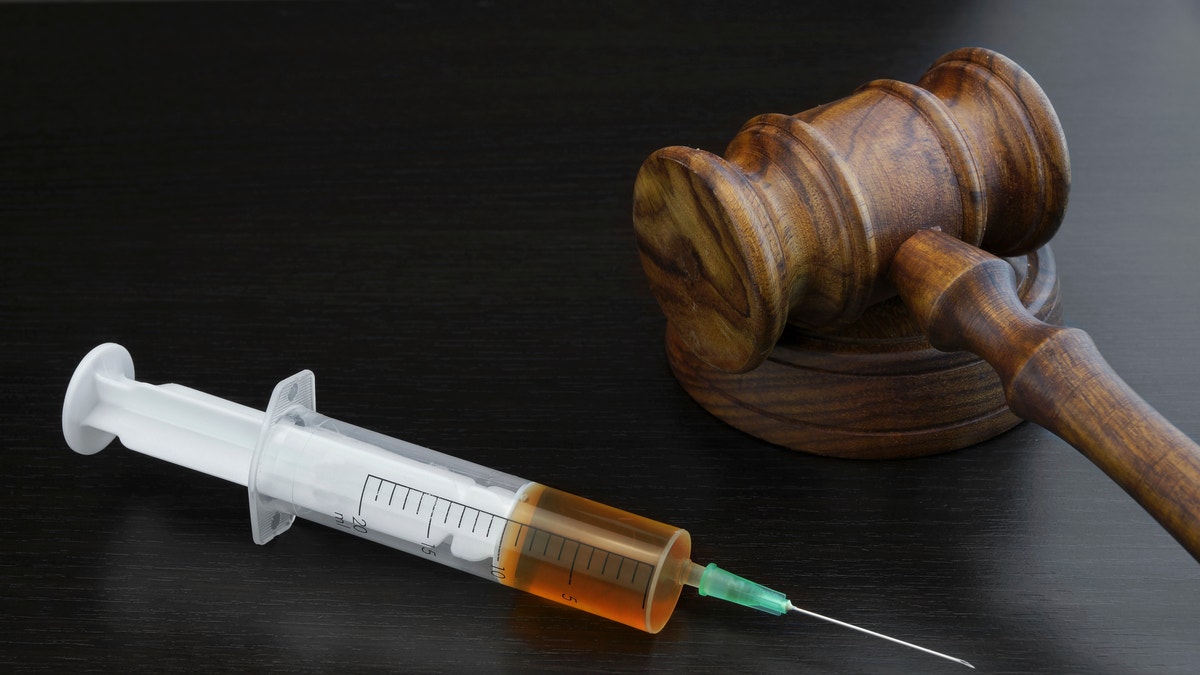 Judges Gavel And Medical Injection Syringe With Brown Liquid On The Black Wood Background, Close-up, Top View