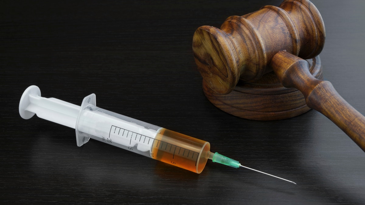 Judges Gavel And Medical Injection Syringe With Brown Liquid On The Black Wood Background, Close-up, Top View