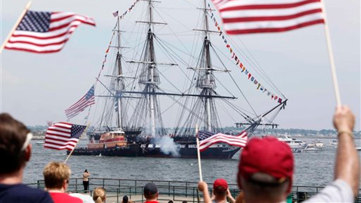 Spectators wave flags as the USS Constitution fires its cannons off Castle Island in Boston on its annual 4th of July turn around in Boston Harbor, Monday, July 4, 2011. (AP Photo/Michael Dwyer)
