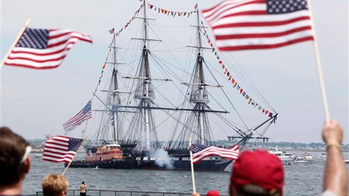 Spectators wave flags as the USS Constitution fires its cannons off Castle Island in Boston on its annual 4th of July turn around in Boston Harbor, Monday, July 4, 2011. (AP Photo/Michael Dwyer)