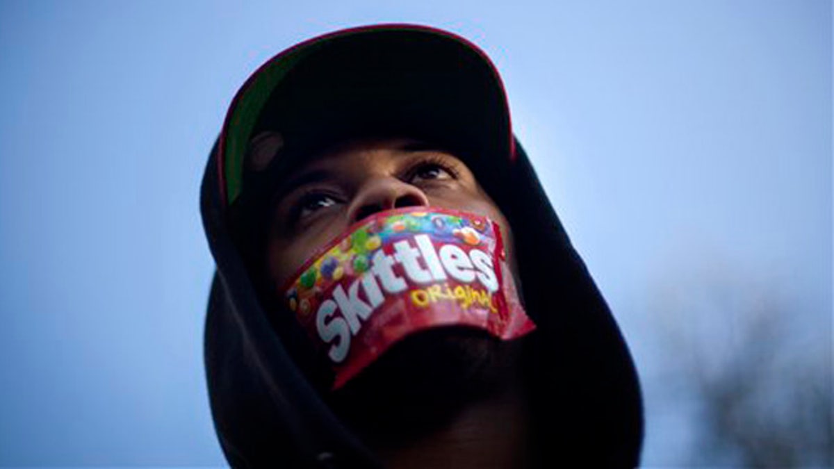 FILE - In this March 26, 2012 file photo, Jajuan Kelley, of Atlanta, wears a Skittles wrapper over his mouth during a rally in memory of Trayvon Martin, the unarmed 17-year-old who was killed by a Florida neighborhood watch captain while returning from a convenience store with a bag of Skittles and an iced tea, in Atlanta. Skittles isn't the first popular food brand to find itself at the center of a major controversy. The terms the Twinkie defense and don't drink the Kool-Aid became part of the vernacular decades ago in the wake of tragic events. More recently, Doritos made headlines when it was reported that the corn chips were Saddam Hussein's favorite snack. (AP Photo/David Goldman, File)